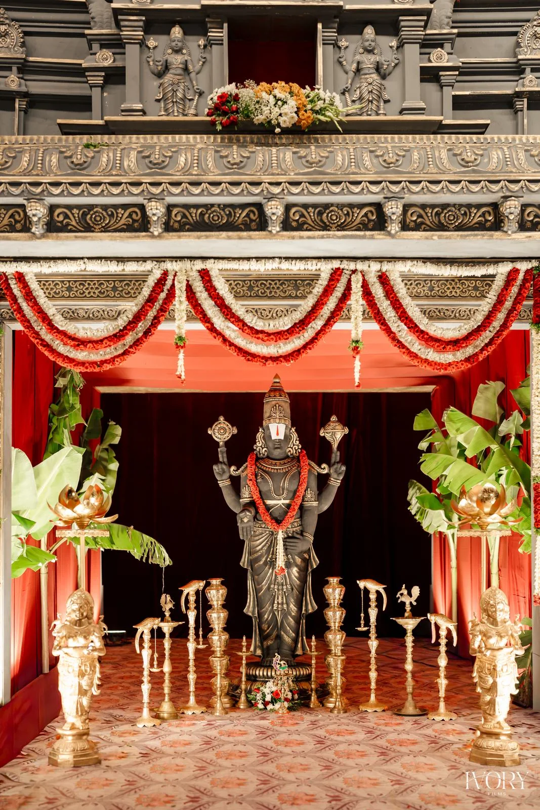 Stone temple facade with red drapes, garlands and a central deity